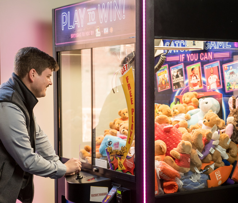 Man plays a claw machine game filled with stuffed animals.